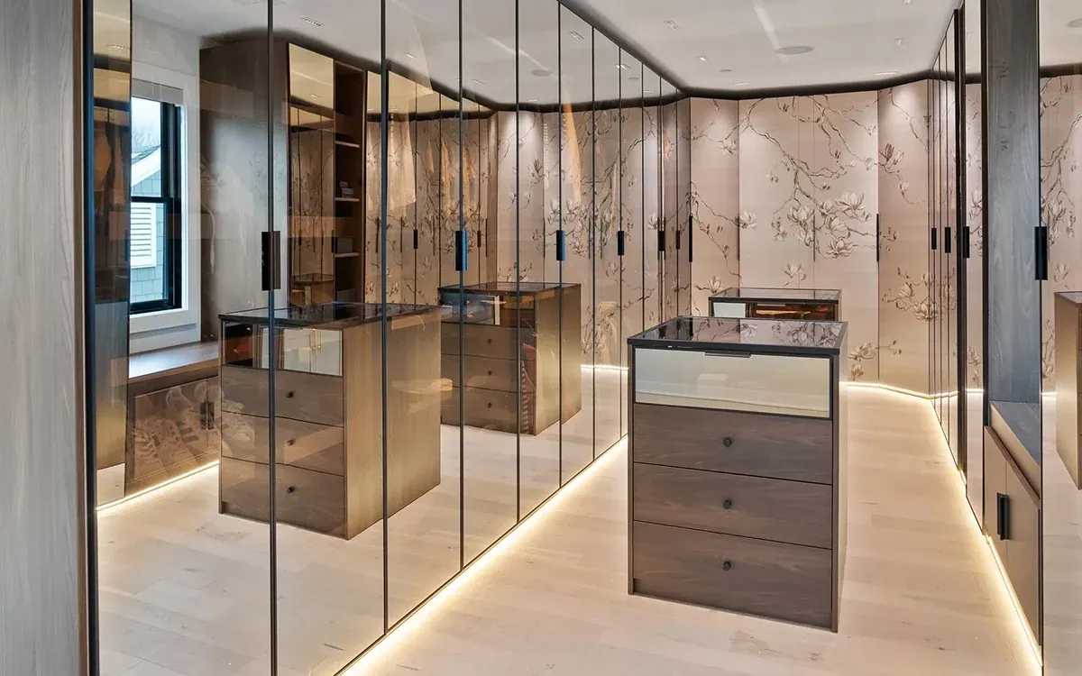 Walk-in closet with glass-front wardrobes, wallpapered doors and a lit drawer island